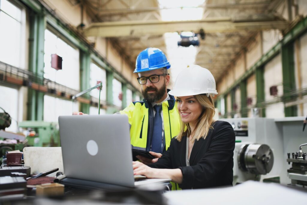 Male and female industrial engineers discussing factory's new machinery project and using laptop.